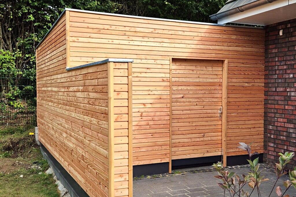 Sichtschutzwand mit integrierter Mülltonnenbox aus Lärchenholz und Flachdach mit Zinkabdeckung – Holzbau der Zimmerei Stange in Kiel